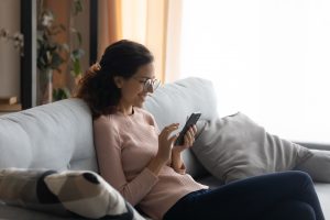 a female on a sofa using her mobile while smiling